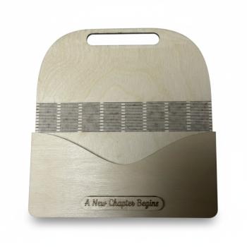 Holz-Umschlag aus hellem Birkensperrholz mit gelaserter Gravur A New Chapter Begins. Der Umschlag liegt dekorativ arrangiert, die natürliche Maserung und feinen Lasercut‑Details sind gut sichtbar. Ideal als Geschenkverpackung für Geld oder Gutscheine zu S